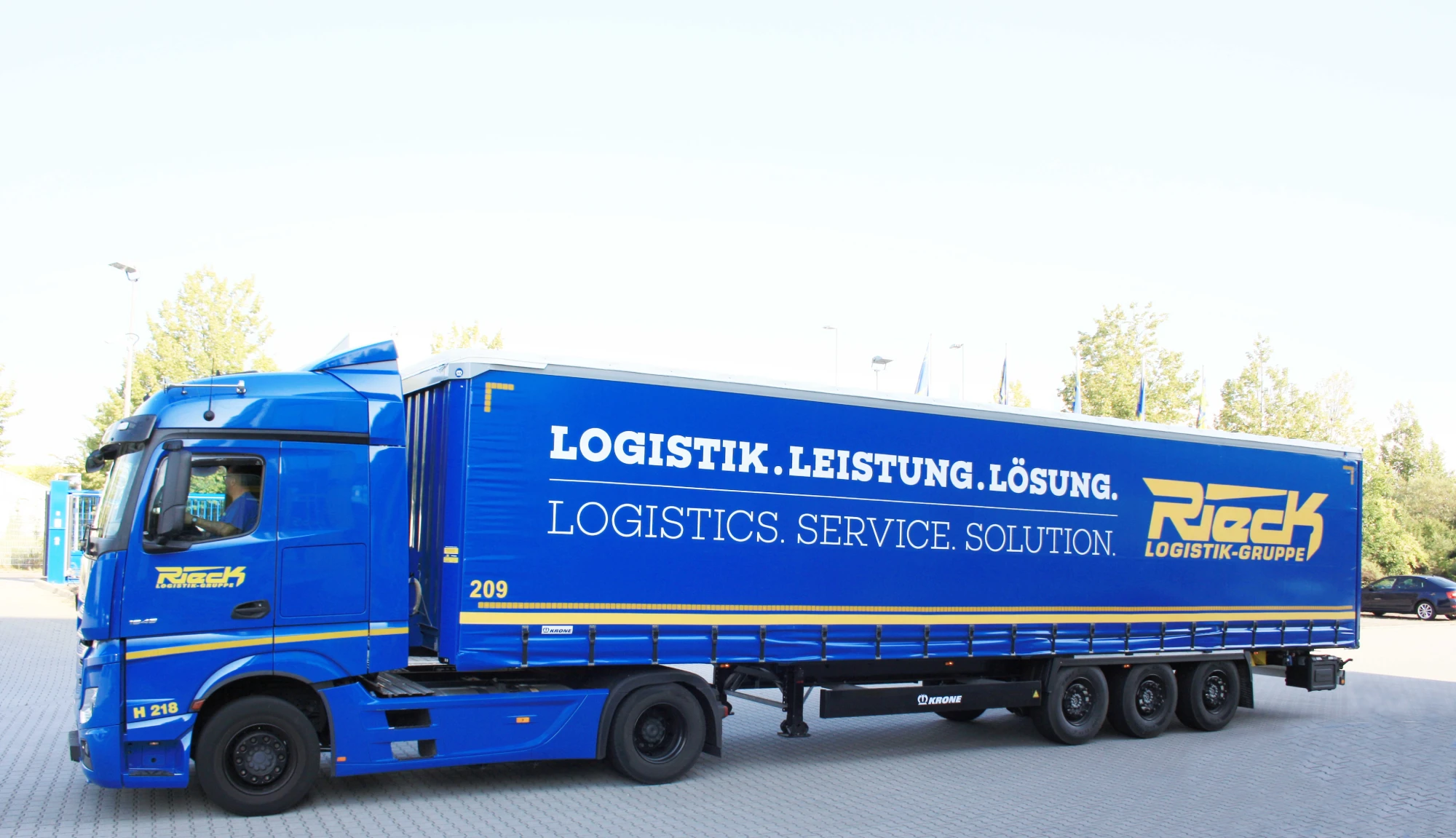 Blauer Sattelzug mit Aufschrift "Logistik. Leistung. Lösung." auf einem Parkplatz.