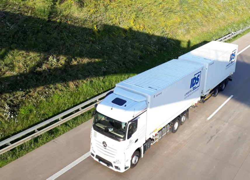 Weißer Sattelzug auf Autobahn neben Grünfläche bei Sonnenschein.