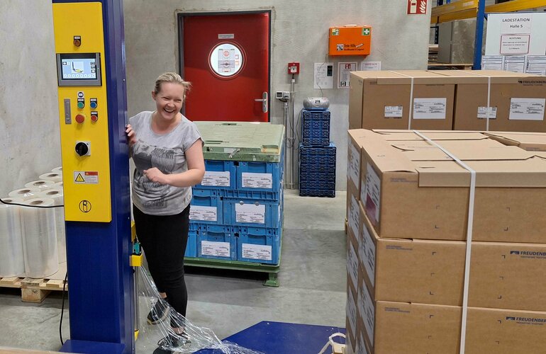 lachende Frau an einer Wickelmaschine in einer Lagerhalle