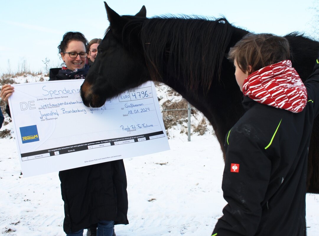 eine Frau mit Ihrem Pferd, die einen Spendenscheck hält.