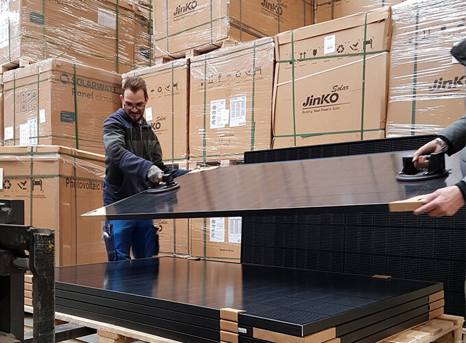 The picture shows two employees lifting a solar module from the pallet.