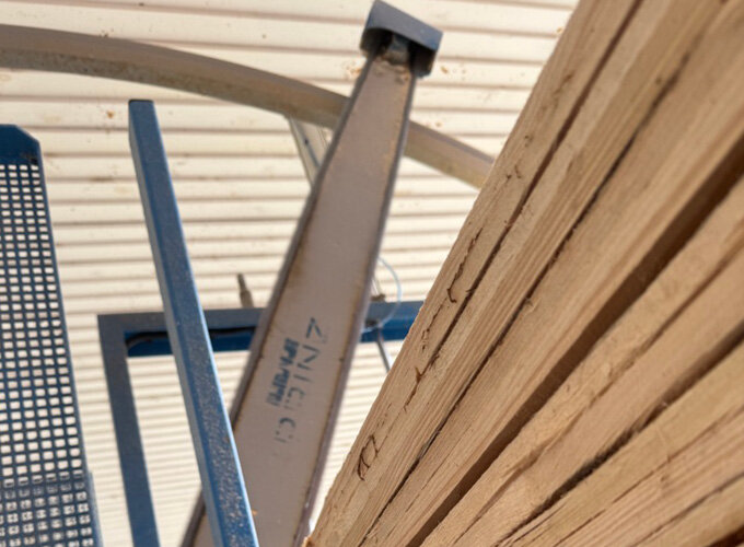 Stapel von Holzlatten neben Metallgestell unter einem überdachten Bereich.