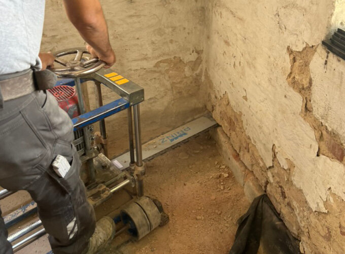 Person bedient eine Maschine zur Bodenbearbeitung in einem Raum mit bröckelnden Wänden.