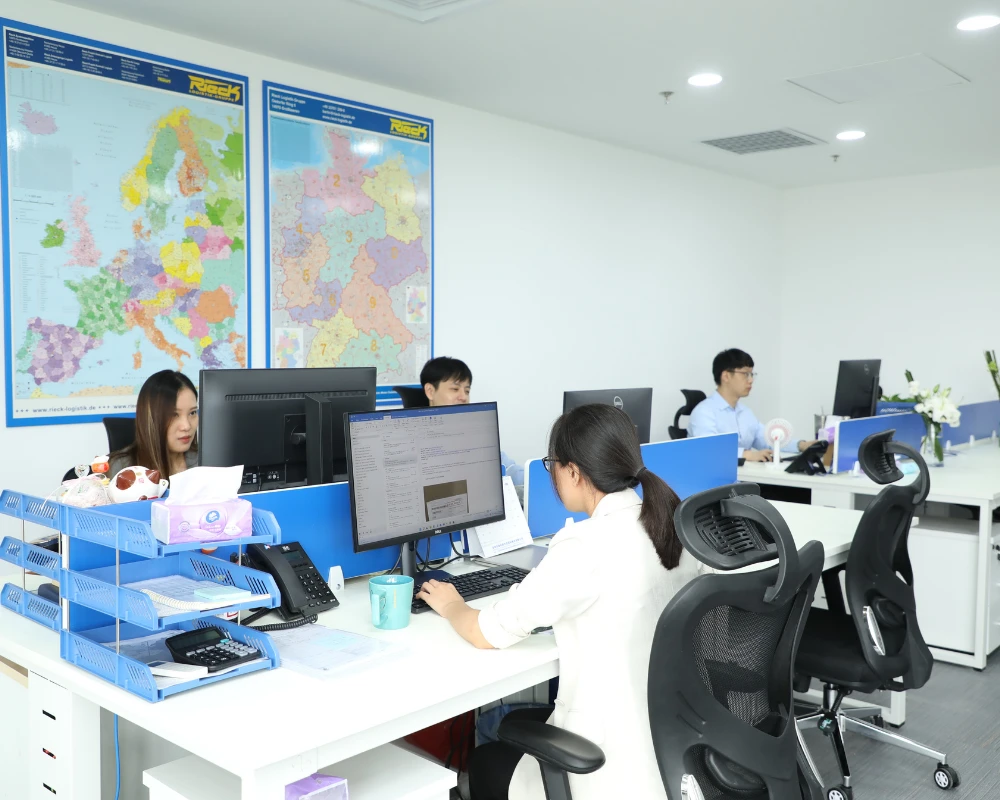 Büro mit mehreren Personen, die an Computern arbeiten, und Karten von Europa an der Wand.