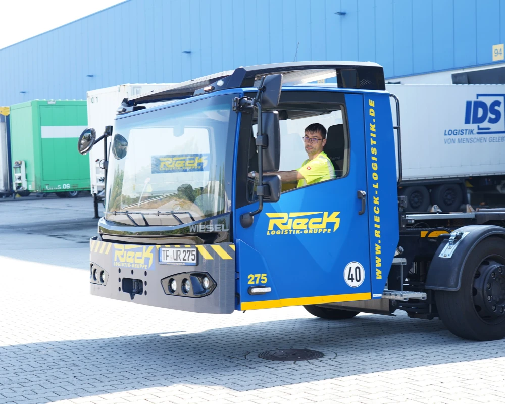 Mann sitzt in einer blauen LKW-Fahrerkabine ohne Fahrgestell auf einem Parkplatz.