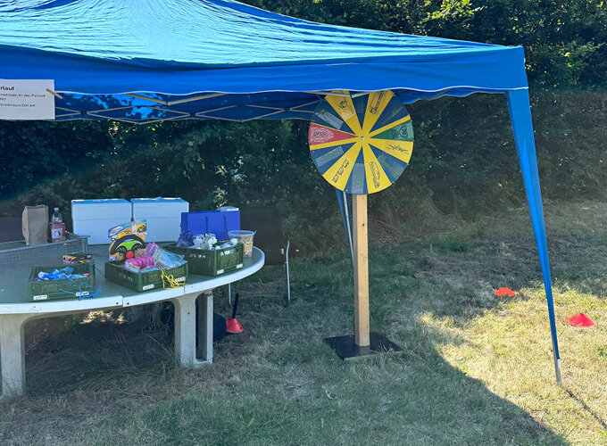 Glücksraddreh unter blauem Pavillon mit Tischen und Spielmaterial im Freien.