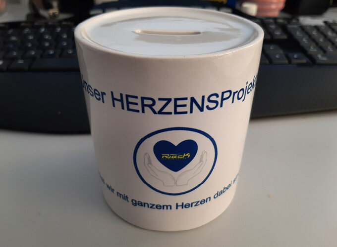 Spardose mit Aufschrift und Herzsymbol auf einem Schreibtisch vor Tastatur.