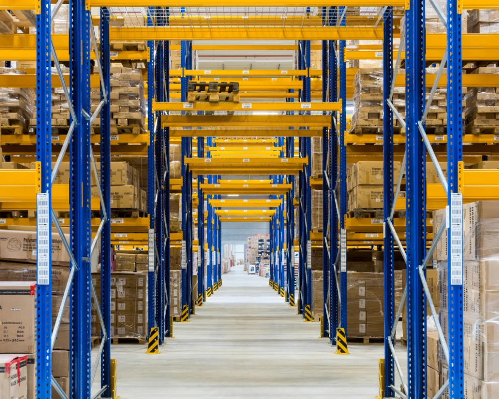 Blick in einen großen Lagerraum mit hohen Regalen voller Kartons und Paletten.
