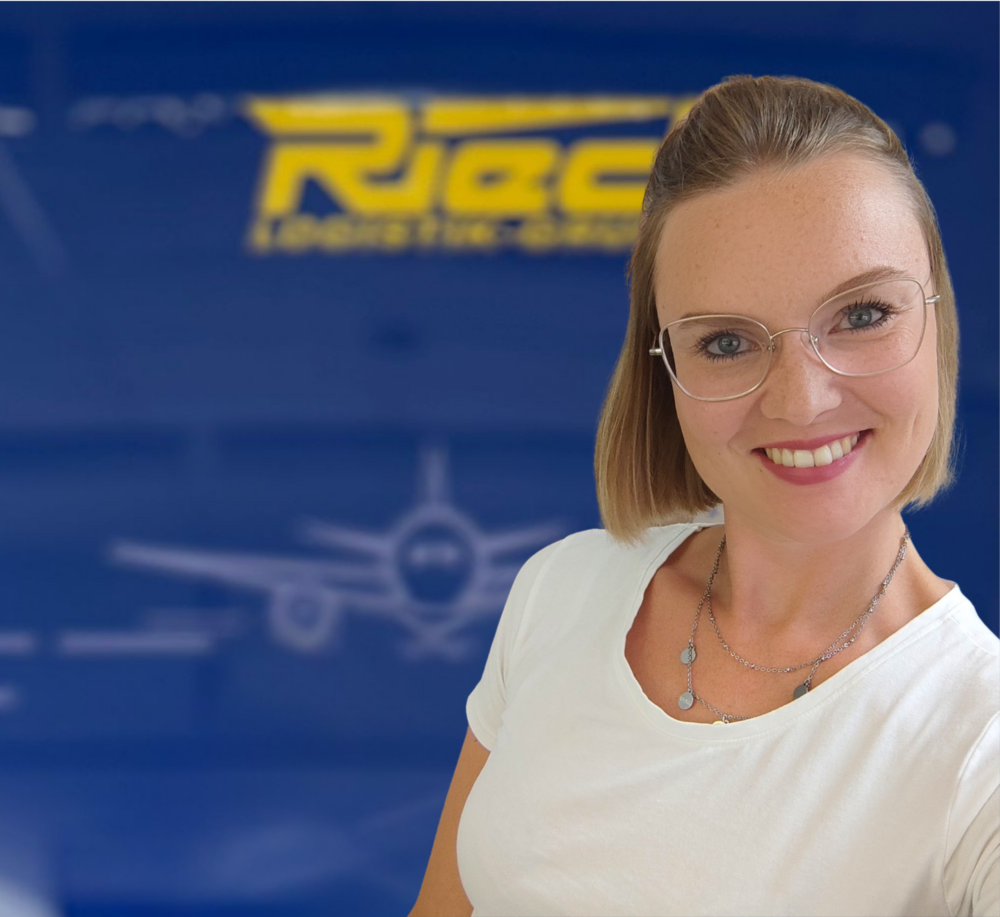 Frau mit Brille und weißem T-Shirt vor blauem Hintergrund mit Flugzeuggrafik und gelbem Schriftzug.
