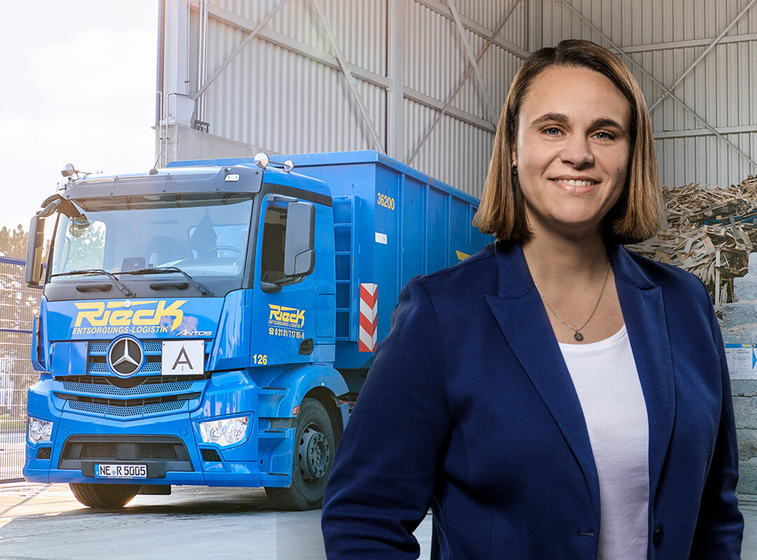 Frau in blauem Blazer vor blauem Müllentsorgungs-LKW in Lagerhalle.