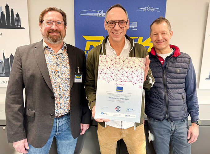 Drei Männer stehen nebeneinander, einer hält eine Urkunde.