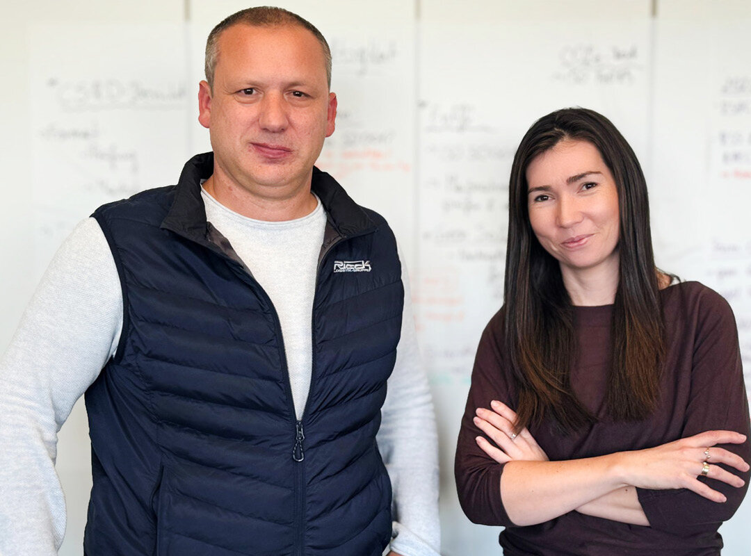 Zwei Personen, ein Mann und eine Frau, stehen vor einer weißen Tafel mit Notizen.
